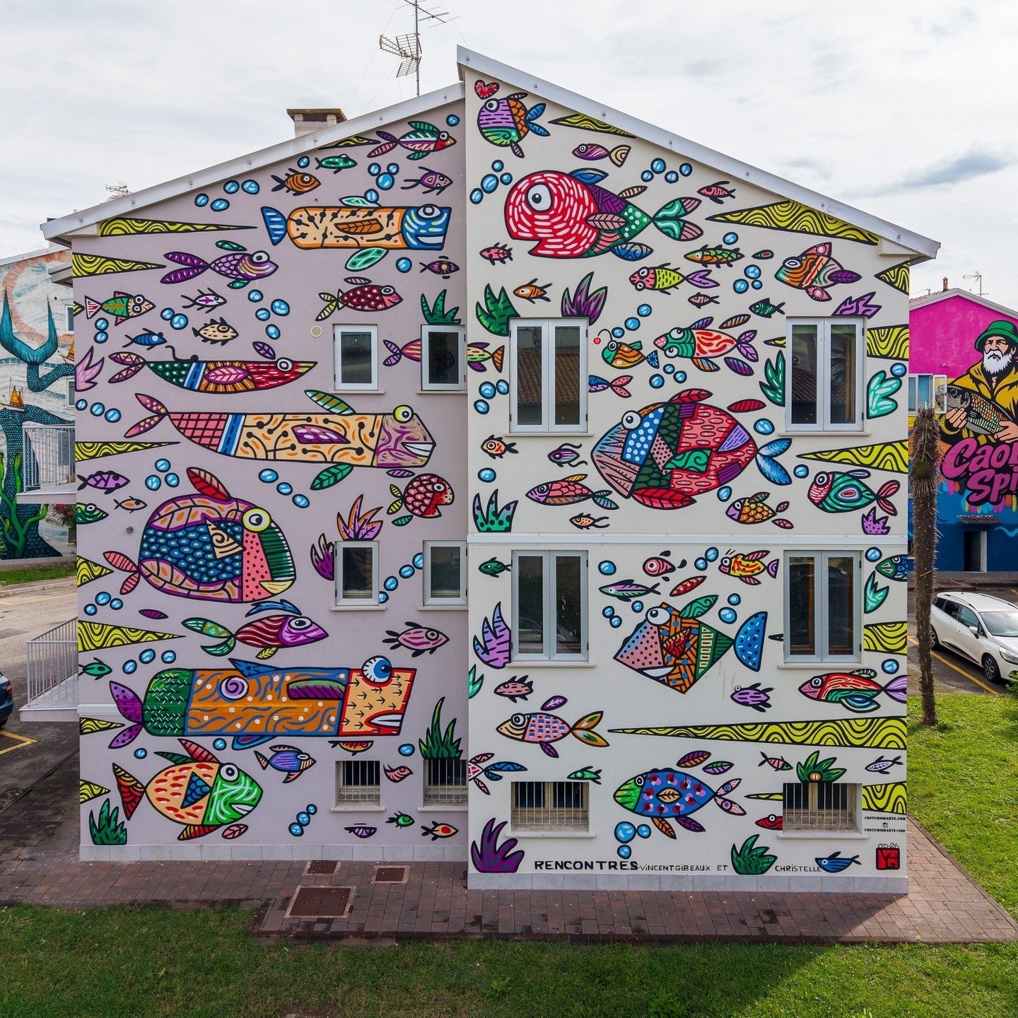 Rencontres, a colorful fish mural by Vincent Gibeaux covering an apartment facade in Caorle, Italy.